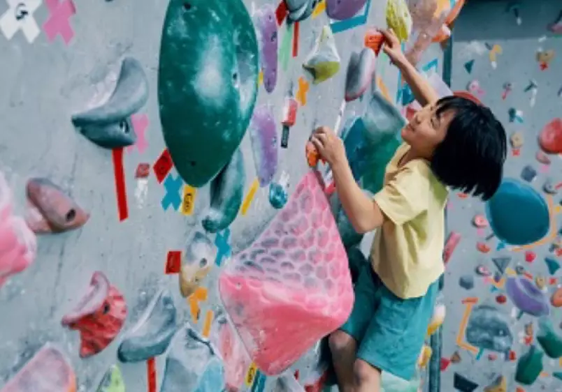 Young girl climbing up a bouldering wall at a sport rock climbing gym