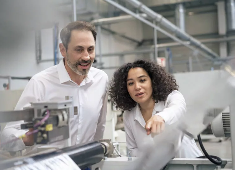 Businesswoman pointing at machine standing by colleague in industry